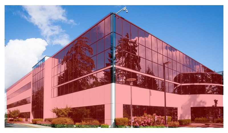 Edificio per uffici con facciata rosa e vetrate a specchio, telecamere sull'angolo del tetto e aiuole fiorite
